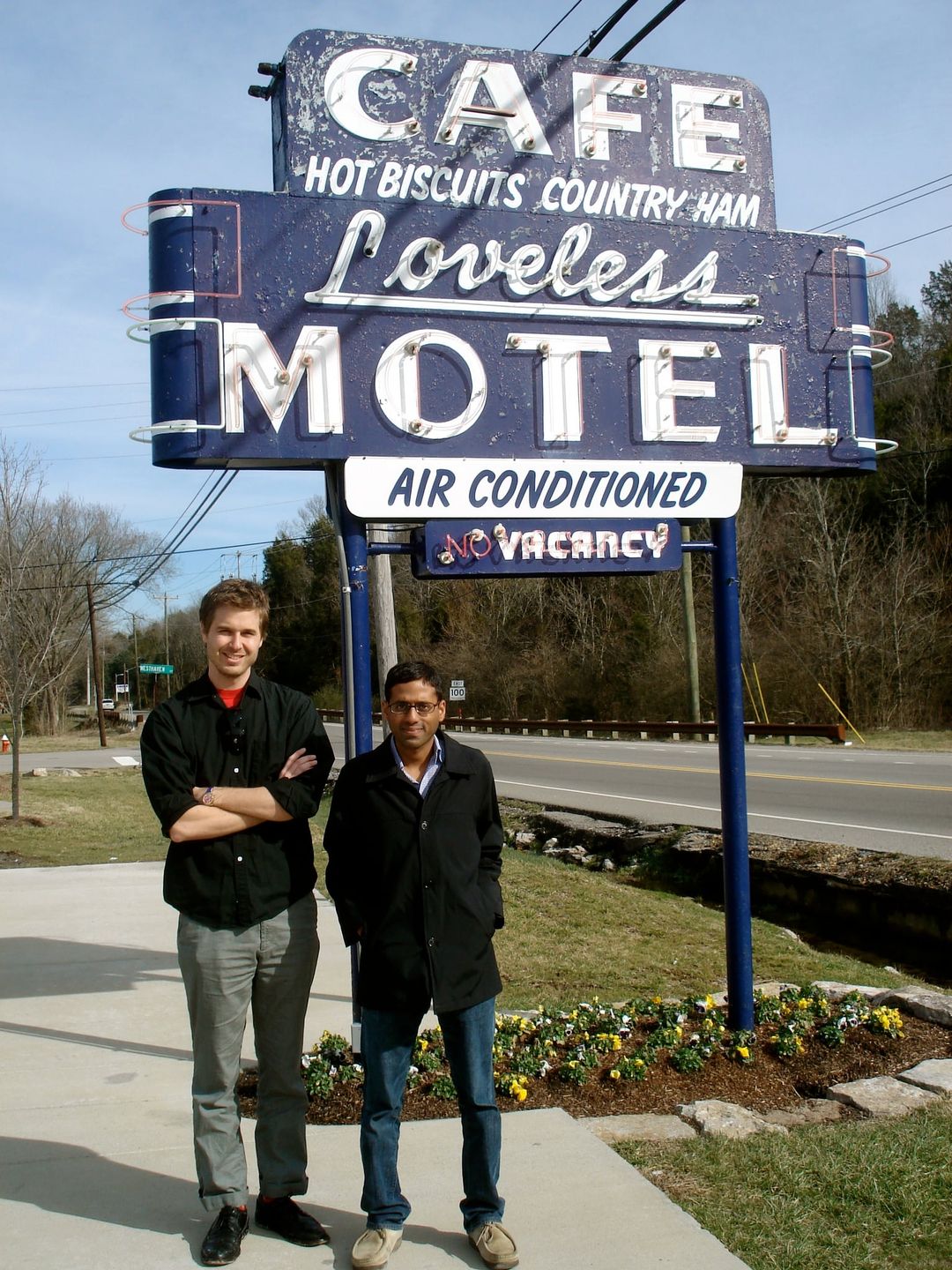 The Foxymorons, a duo, stand beneath the vintage neon Loveless Motel sign on a sunny day.